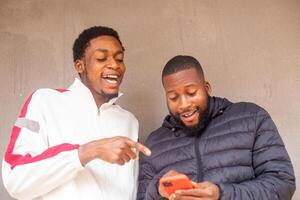 two young african men standing outside and delighted while using there smart phone photo