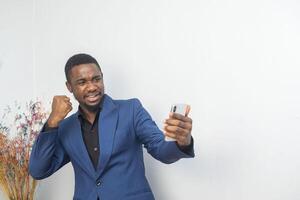 portrait of cheerful young black guy sending message on mobile phone. Happy African-American man using smartphone, enjoying chatting online, messaging in social networks photo