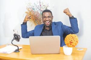Handsome Afro American businessman in classic suit is using a laptop and smiling while working in office photo