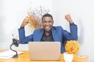 Handsome Afro American businessman in classic suit is using a laptop and smiling while working in office photo