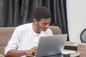 Young man smiling as he reads the screen of a laptop computer while relaxing on a comfortable couch at home photo