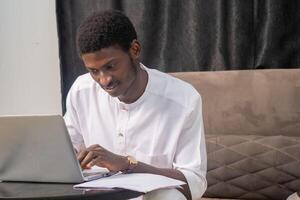 Young man smiling as he reads the screen of a laptop computer while relaxing on a comfortable couch at home photo