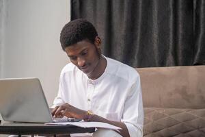 Young man smiling as he reads the screen of a laptop computer while relaxing on a comfortable couch at home photo