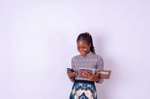Young fun girl woman of African American ethnicity student hold books use mobile cell phone isolated on plain white background. photo