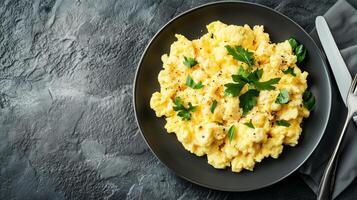 Plate of scrambled eggs with visible seasoning, placed beside a fork and knife, meal photography photo