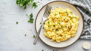 Plate filled with scrambled eggs, placed on a clean surface beside a fork, meal photography photo
