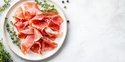 Prosciutto slices displayed on a white plate, with a sprig of fresh herbs, meal photography photo