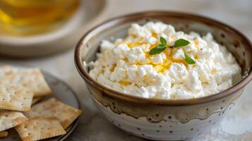 Bowl of cottage cheese with honey drizzle next to a plate of crackers, food setting photo