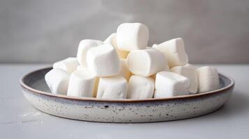 Plate of plain white marshmallows stacked neatly on a neutral background, food setting photo