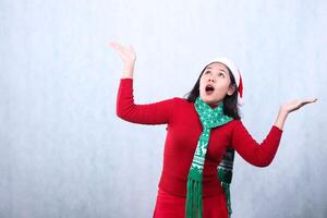 portrait of woman wearing red sweater party wear with Santa hat and scarf, surprised looking up and both hands raised up, celebrating Christmas and New Year isolated on white background photo