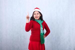 Asian woman gesture wearing red sweater party wear with Santa hat and scarf, left slant hold waist and touch and look right, celebrating christmas and new year isolated on white background photo