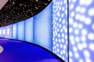 Bright blue LED screens illuminate a vibrant tech exhibition booth with dark blue backdrops and red branding in a modern setting photo