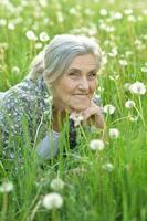 Portrait of a beautiful senior woman in green field with dandelions photo
