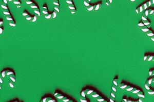 Flat lay Christmas composition with frame of candy canes on a green background. photo