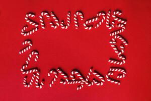 Flat lay Christmas composition with frame of candy canes on a red background. photo