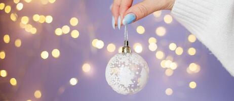 womans hands holding Christmas toy ball on purple blurred bokeh background photo