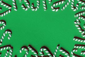 Flat lay Christmas composition with frame of candy canes on a green background. photo