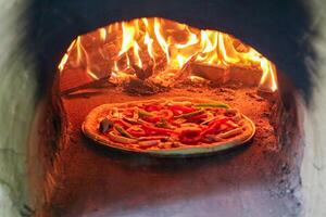 A traditional oven for cooking and baking pizza with a shovel. Firewood burning in the oven. Wood-fired oven. Image of a brick pizza oven with fire. photo