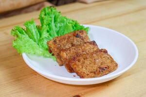 Tempe Bacem is a traditional food of Central Java, the tempeh is flavored with brown sugar and then fried, served on wicker bamboo plate photo