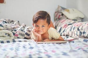 niñito chico jugando con digital inalámbrico tableta computadora a hogar. bebé niño creciente con en línea aplicaciones niño y electrónico dispositivos concepto. retrato de niñito con teléfono inteligente foto