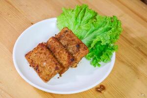 Tempe Bacem is a traditional food of Central Java, the tempeh is flavored with brown sugar and then fried, served on wicker bamboo plate photo