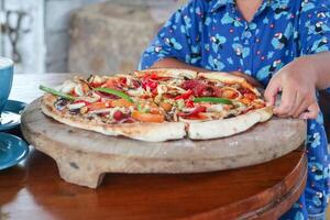 asiático chico contento a comer Pizza con un caliente queso es derritiendo y extensión en un de madera almohadilla. aislado en blanco fondo, escoger atención punto. foto