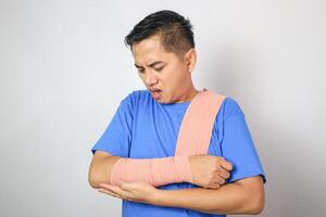 Handsome young asian man with broken arm in soft splint suffering a sore arm isolated on grey background, accident insurance concept. photo