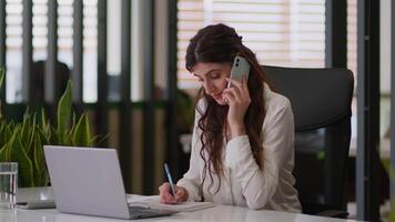 Caucasian business woman busy female businesswoman office girl planner organizer talking mobile phone conversation cellphone chatting client order e-commerce write notebook manage tasks work laptop video