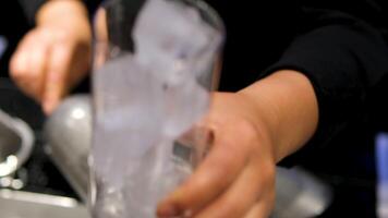 bartender fills glass with ice Preparation of an alcoholic beverage from beginning to moment of serving. Pouring ice, mixing liquids and soda, adding orange. Close-up of the hands. video
