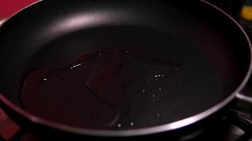 Cook pours sunflower oil into a frying pan, top view. Kitchen pan stands on brown boards, vegetables around it, and oil is poured into it for frying. Slow motion of oil pouring into a frying pan. video