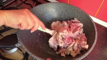 Fried slices of fresh beef in boiling oil stirred with a steel ladle in cast iron wok frying pan, red meat stewed on high heat on a gas stove, close-up. video