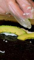 add avocado to sushi Chef wear black gloves carefully prepares sushi rolls, carefully adding avocado slices to filling, concept skill and precision of Japanese culinary traditions. video