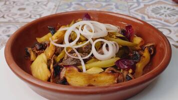 Fried potatoes with mushrooms and onion rings in clay plate spinning round on table video