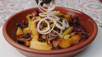 Fried potatoes with mushrooms and onion rings in clay plate spinning round on table video