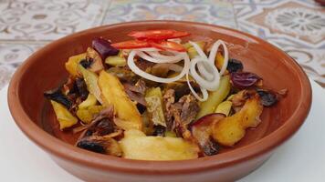 Fried potatoes with mushrooms and onion rings in clay plate spinning round on table video
