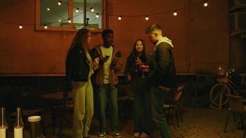 A cozy gathering of friends enjoying drinks under string lights at an outdoor space during a warm evening video