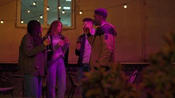Friends enjoying a festive gathering at an outdoor location with string lights and drinks in hand during the nighttime video