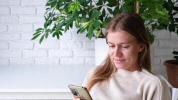 woman using smartphone at home with lots of plants, thoughtfully typing a message and looking photos video