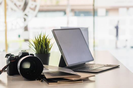 A DSLR camera is placed next to the computer on the desk as the photographer prepares to transfer the images from the camera onto the computer and edit the images for the customer. photo