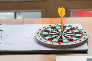 concept of setting business goals or aiming at clear business goals using dartboard and darts as representatives for aiming at precise goals. darts that stuck at center of target are placed on table. photo