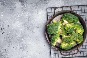 Green fresh broccoli pieces in a steel tray. grey background. top view photo