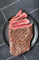 Grilled Flap or Flank Steak, sliced on a plate. Black background. Top view photo