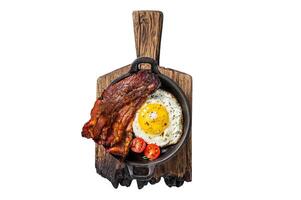 English breakfast with fried egg and bacon in cast iron pan. Isolated on white background, top view. photo