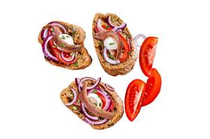 Spanish tapas on bread with olive oil, herbs, tomatoes and spicy anchovy fillets. Isolated on white background, top view. photo