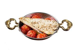 Roasted Haddock fish fillet in skillet with tomato and potato. Isolated on white background. Top view. photo