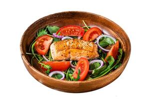 Salmon steak salad with green leaves arugula, avocado and tomato in a wooden plate. Isolated on white background, top view. photo