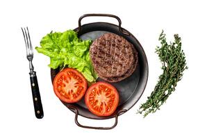 Tasty grilled burger beef patty with tomato, spices and lettuce in kitchen tray. Isolated, white background. photo