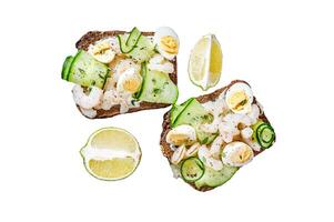 Fresh toasts with shrimp, prawns, quail eggs and cucumber on rye bread. Isolated on white background, Top view. photo