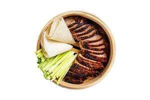 Peking Duck in bamboo steamer served with cucumber, green onion, and wheaten chinese pancakes. Isolated on white background. photo