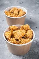 Crunchy chicken popcorn bites in a basket from fastfood. Gray background. Top view photo